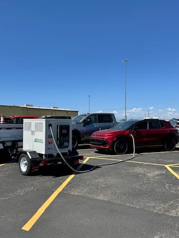 Trailer-mounted charger connected to a red electric vehicle in a parking lot